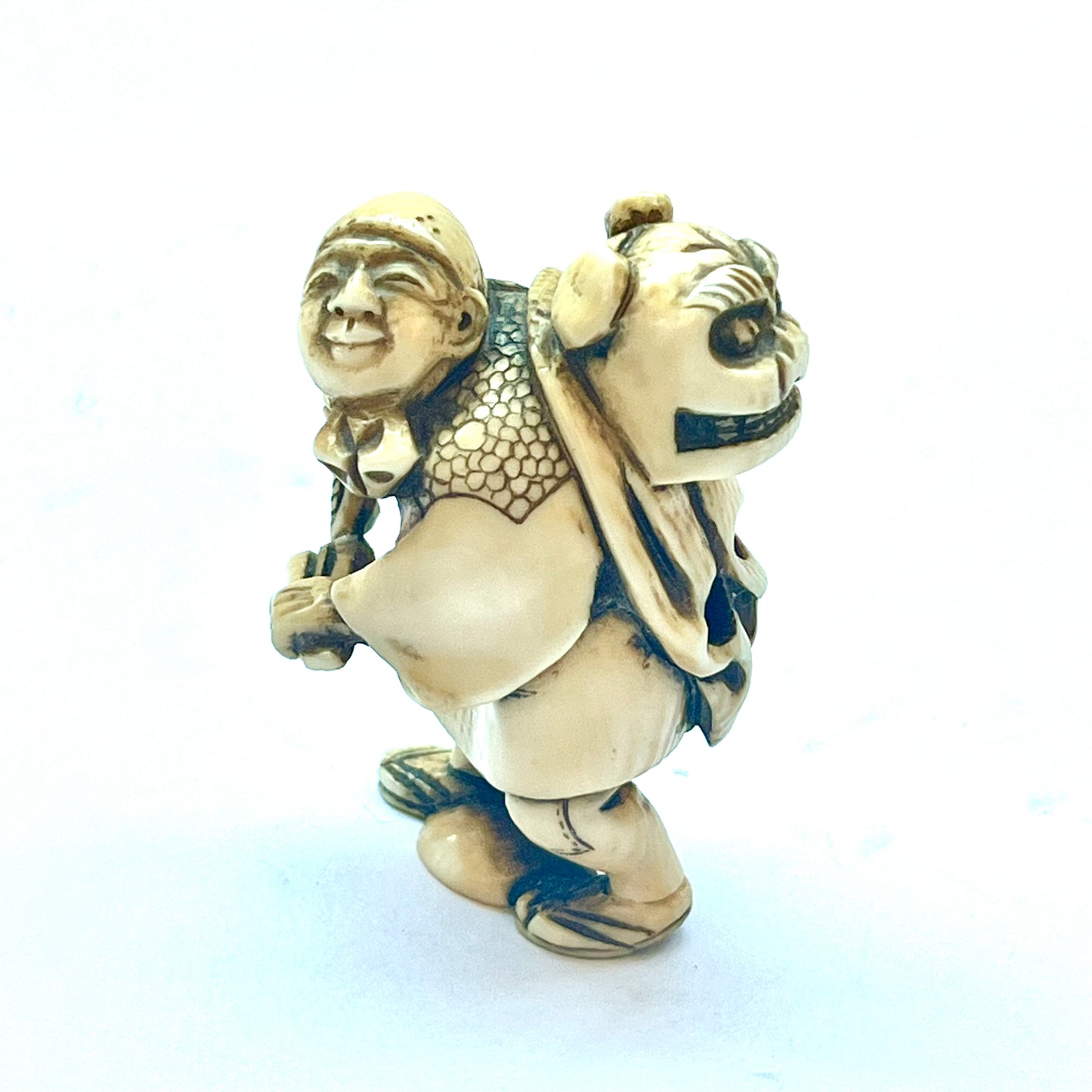 Antique Japanese Meiji Period ivory netsuke depicting an old man carrying a shishi, signed by Hideyuki