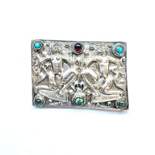Broche antiguo de plata tibetana con piedras semipreciosas y motivos de deidades repujados.