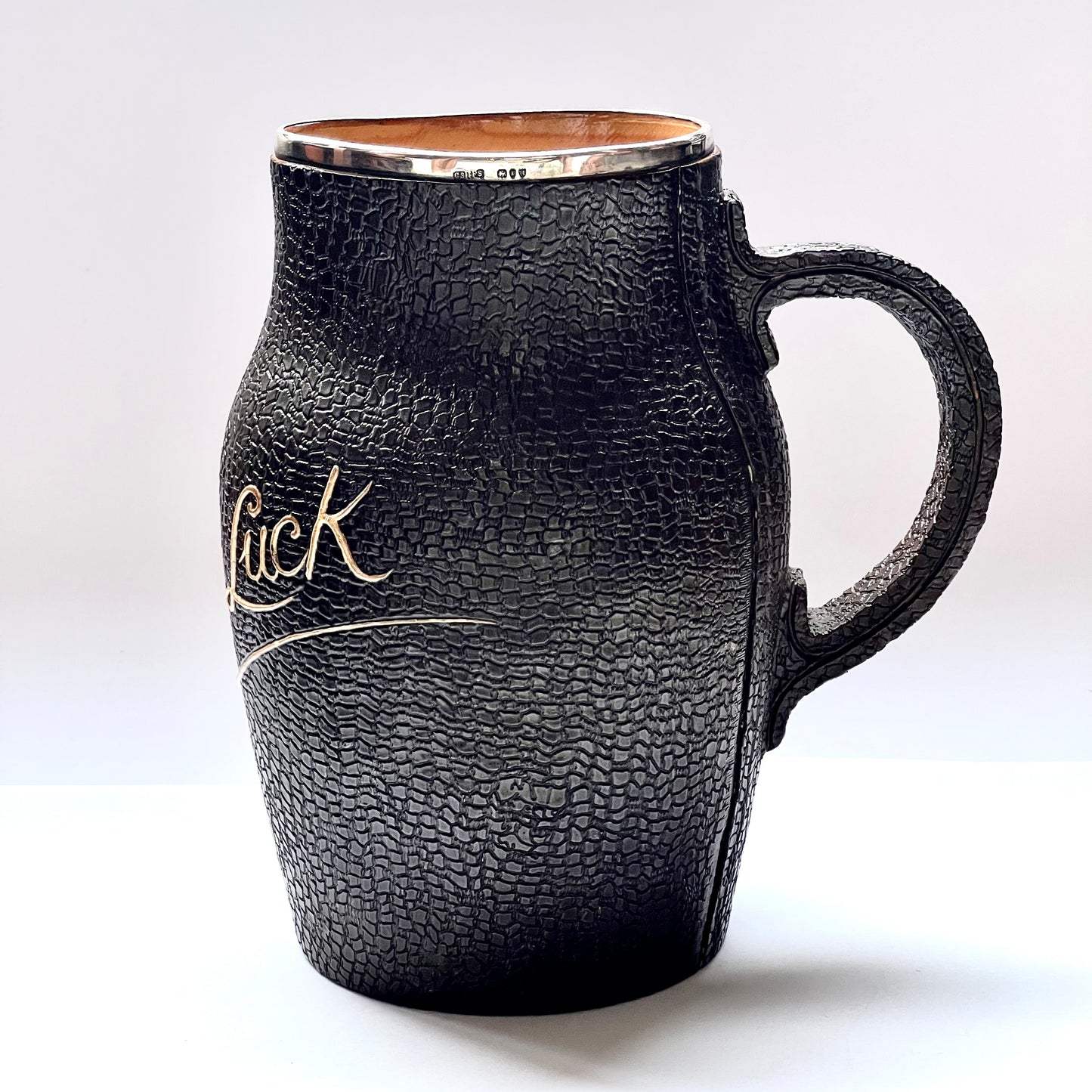 Victorian Doulton Lambeth Leather Ware Slaters blackjack jug with Sterling Silver Rim, marked for London, 1892, Cornelius Desormeaux Saunders & James Francis Hollings (Frank) Shepherd.